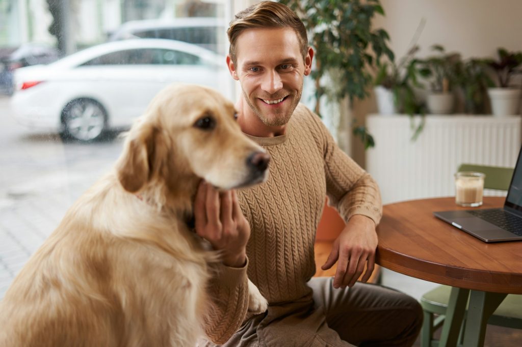 Close up portrait of smiling handsome european man with his dog in a cafe. Guy pets his golden