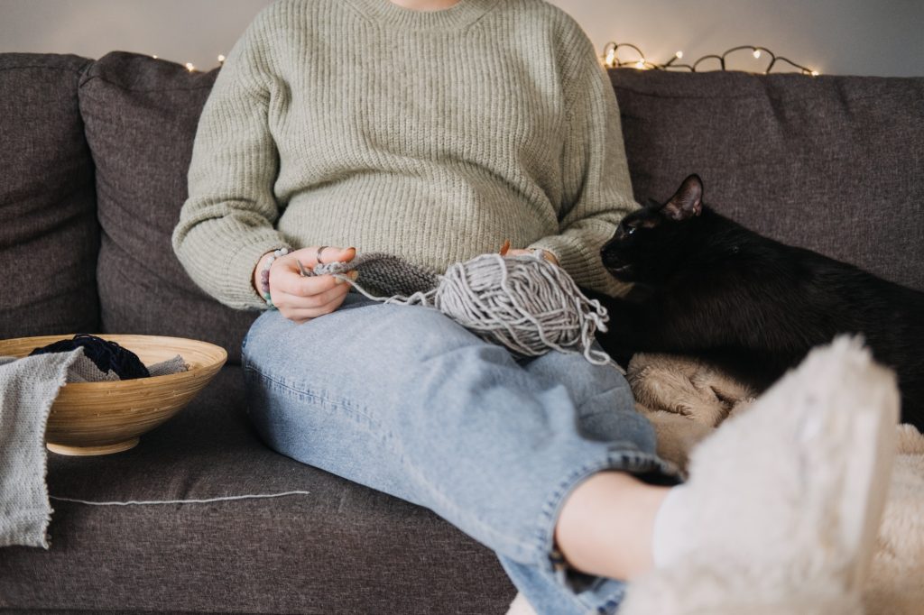 Woman knitting with black cat on sofa, embracing cozy downtime. Relaxation, companionship, digital